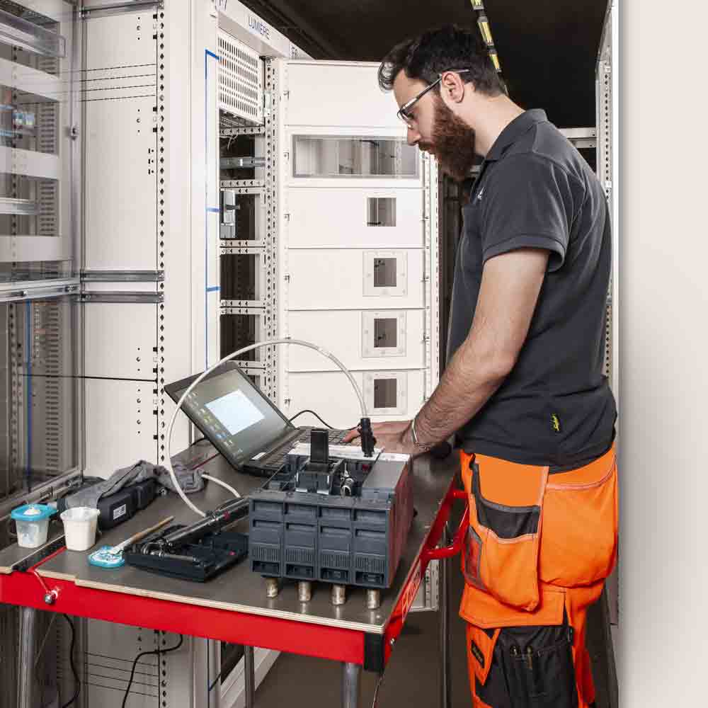Jeune employé de Flückiger utilisant un ordinateur pour la maintenance de systèmes électriques, expertise en action.