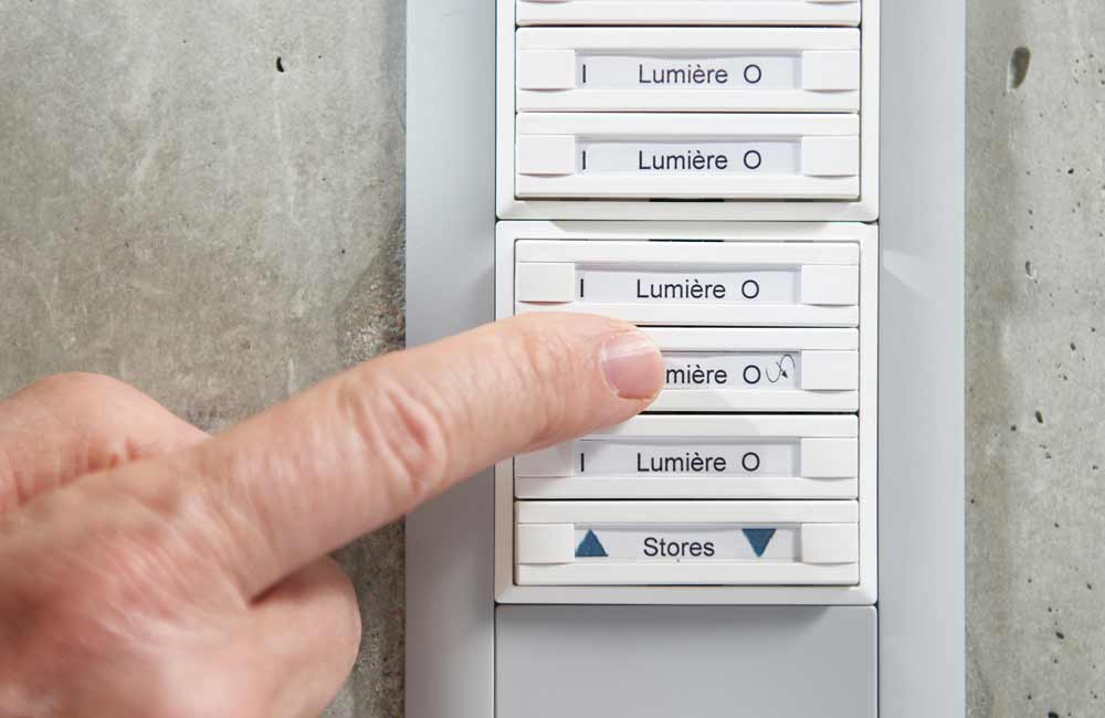 Détail d'un panneau de commande avec interrupteurs pour lumière et stores, démontrant les solutions de domotique appliquées par Flückiger dans la gestion technique de bâtiment.
