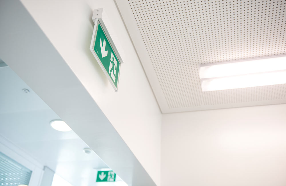 Éclairage de secours au plafond illuminant une signalisation de sortie de secours avec détection d'incendie, soulignant les normes de sécurité de Flückiger.