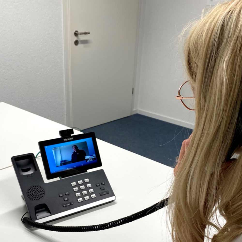 Employée utilisant un téléphone fixe moderne avec écran pour une vidéoconférence dans une salle de conférence, illustrant les solutions de télécommunication de Flückiger.