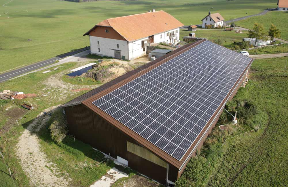 Vue aérienne d'une vaste installation agricole équipée de panneaux solaires près d'une ferme, montrant l'engagement de Flückiger envers les solutions énergétiques durables en milieu rural.