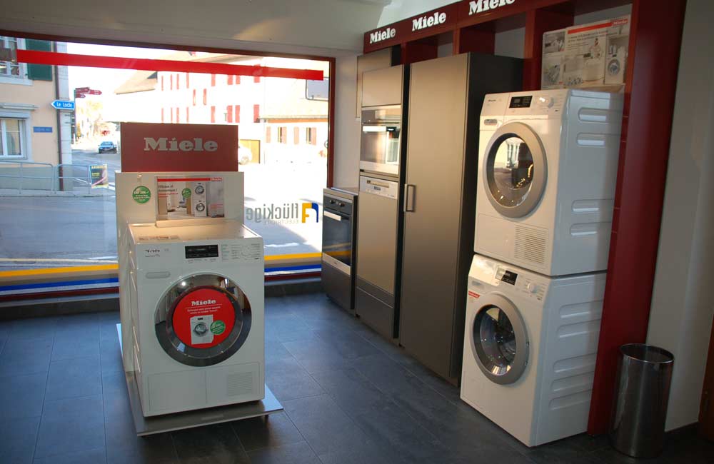 Vitrine d'exposition aux Ponts de Martel présentant des fours, des machines à laver, des sèche-linges et un réfrigérateur, illustrant la variété des appareils disponibles chez Flückiger.
