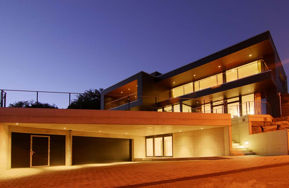 Grande maison avec garage automatique, éclairage d'ambiance direct et indirect, et stores automatisés, démontrant la modernité des installations électriques de Flückiger.