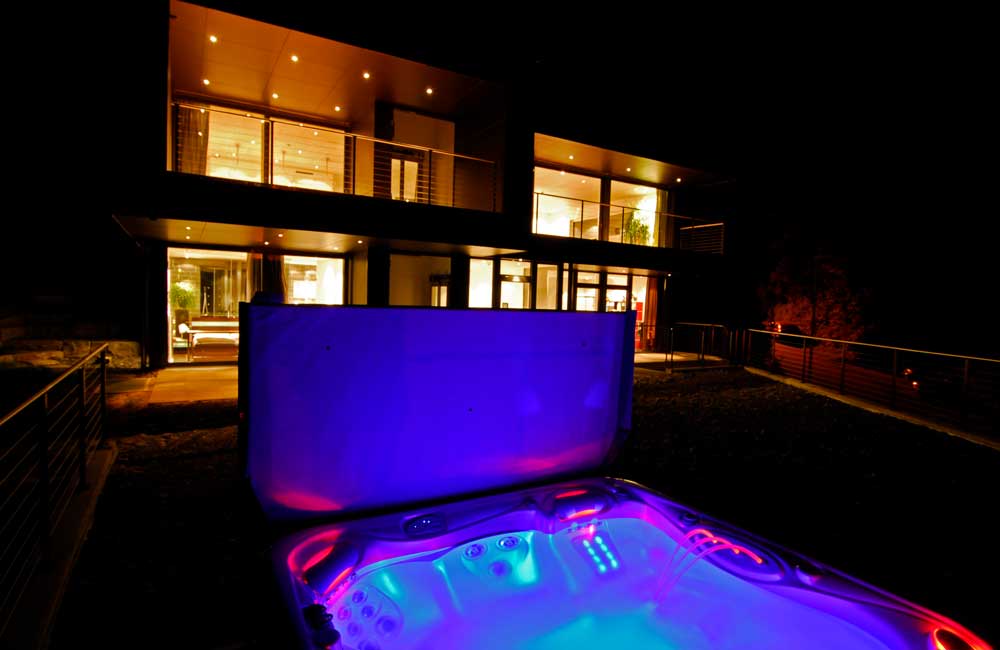 Maison avec éclairage extérieur sophistiqué et stores automatiques près d'une piscine ou d'un jacuzzi, montrant les solutions d'aménagement extérieur de Flückiger.