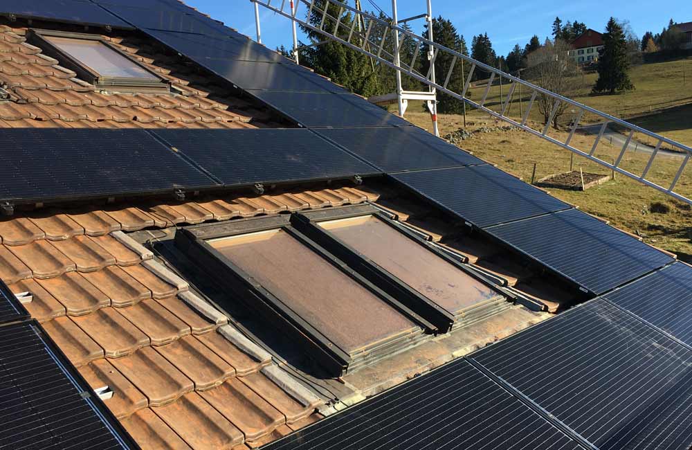 Toit avec fenêtres équipé de panneaux solaires, installation en cours avec un échafaudage visible, reflétant l'expertise de Flückiger dans la mise en place de systèmes photovoltaïques adaptés à la ruralité.